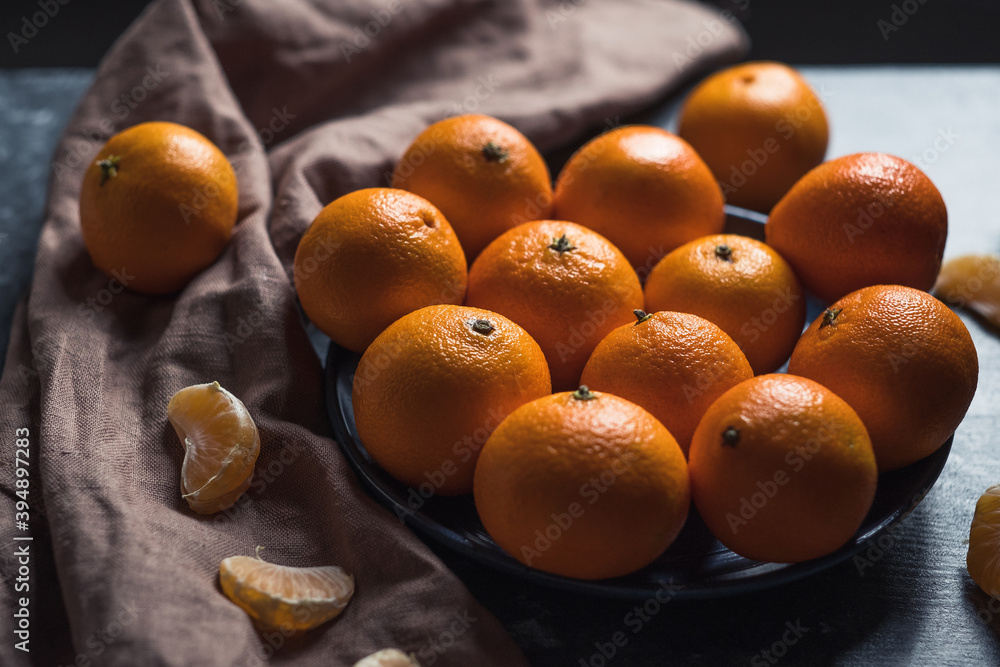 Round fresh ripe tangerines in a plate on a brown textile napkin. Low key. Vitamin C concept. Round fresh ripe tangerines in a plate on a brown textile napkin. Low key. Vitamin C concept.