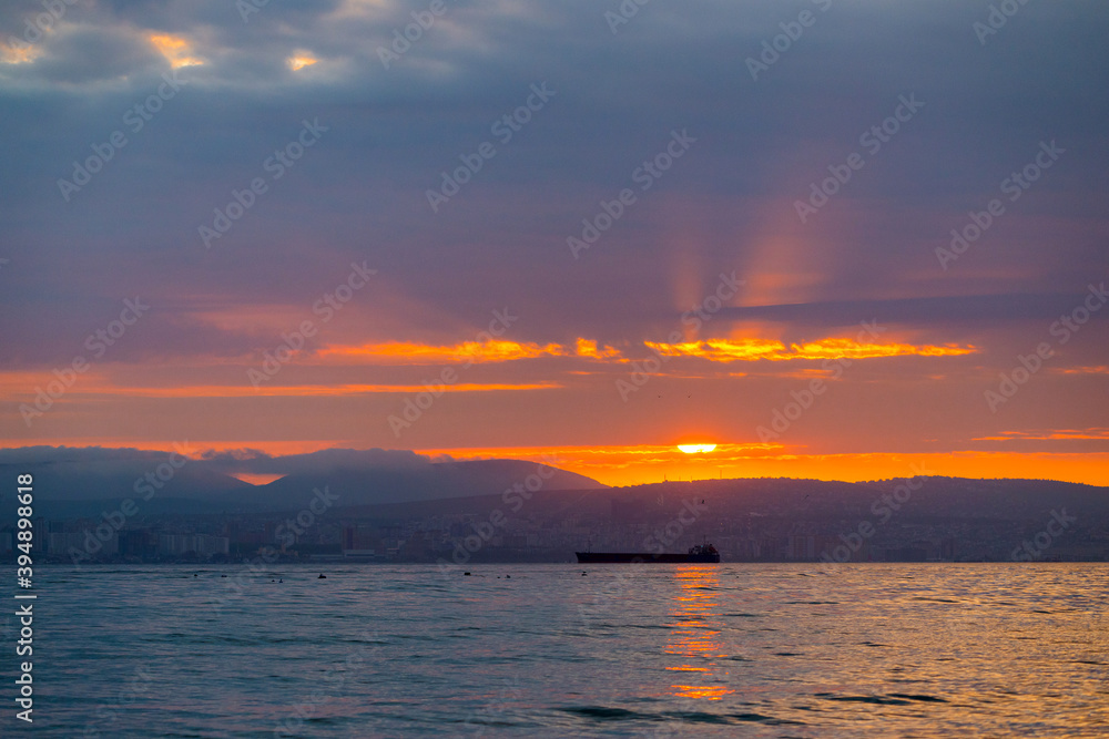 Obraz premium Beautiful sunset amongst the clouds. The sun rays are simply beautiful. City, mountains and ships in sea
