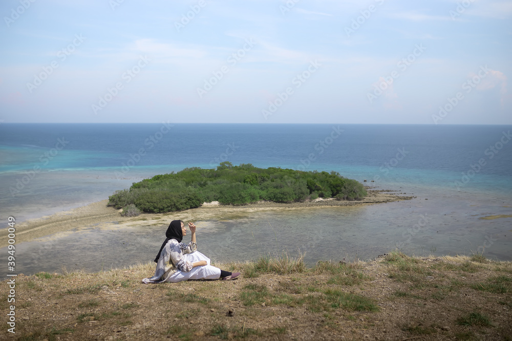 A young traveler girl sits on the edge of a hill on Balanan Beach and enjoys the beautiful sea view of Baluran National Park. Young girls love wildlife, travel, freedom. A young traveler girl sits on the edge of a hill on Balanan Beach and enjoys the beautiful sea view of Baluran National Park. Young girls love wildlife, travel, freedom.