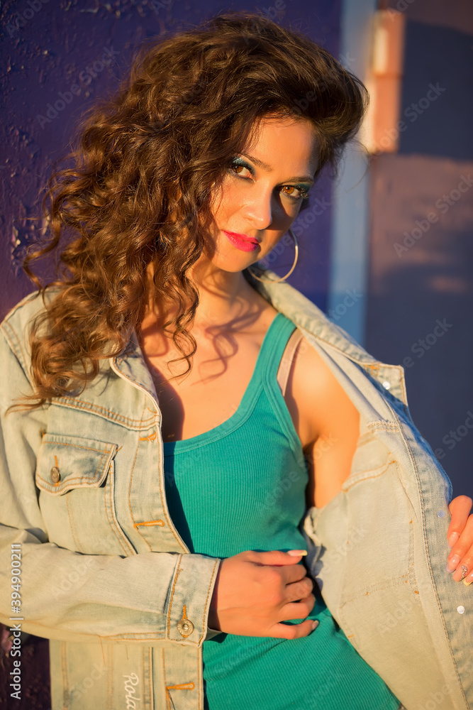 Beautiful young woman in a denim jacket on the background of a peeled purple wall. Girl with bright makeup in the style of the eighties on the street. Beautiful young woman in a denim jacket on the background of a peeled purple wall. Girl with bright makeup in the style of the eighties on the street.