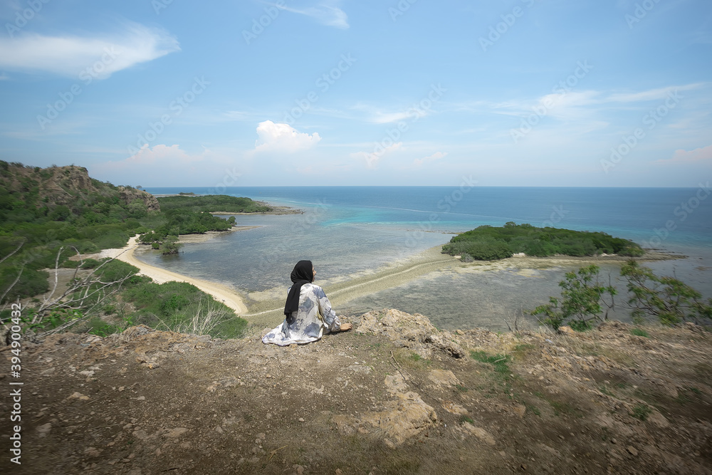 A young traveler girl sits on the edge of a hill on Balanan Beach and enjoys the beautiful sea view of Baluran National Park. Young girls love wildlife, travel, freedom.