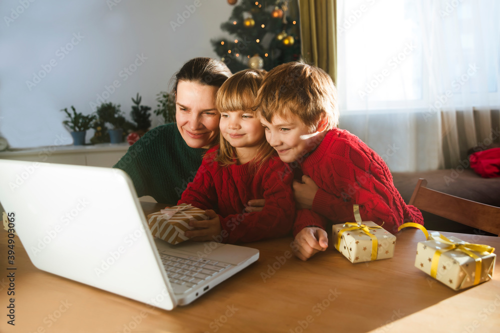 Family mom and two kids with a Christmas gift using a laptop communicates with their friends on video call using webcam. stays at home for Christmas holidays. Family mom and two kids with a Christmas gift using a laptop communicates with their friends on video call using webcam. stays at home for Christmas holidays.