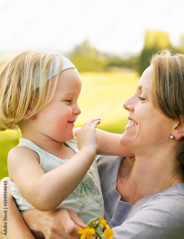 Mother holding buttercups and little girl while smiling at each other, standing in a field Mother holding buttercups and little girl while smiling at each other, standing in a field