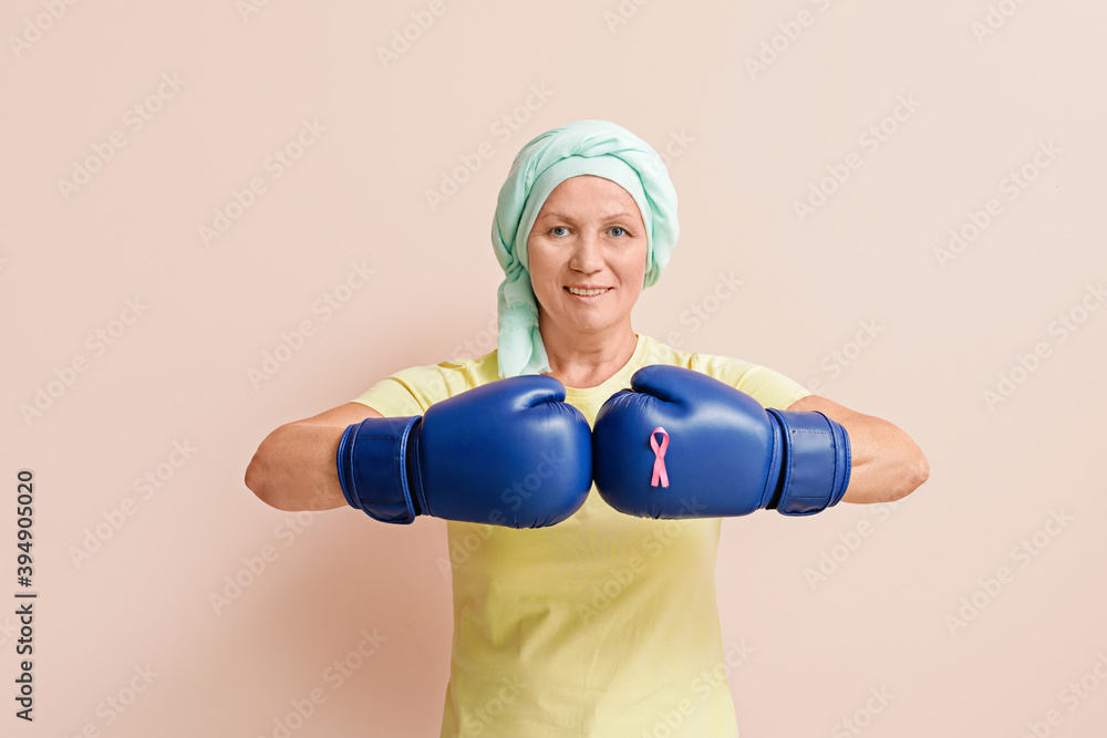Mature woman after chemotherapy in boxing gloves on color background. Fight against breast cancer Mature woman after chemotherapy in boxing gloves on color background. Fight against breast cancer