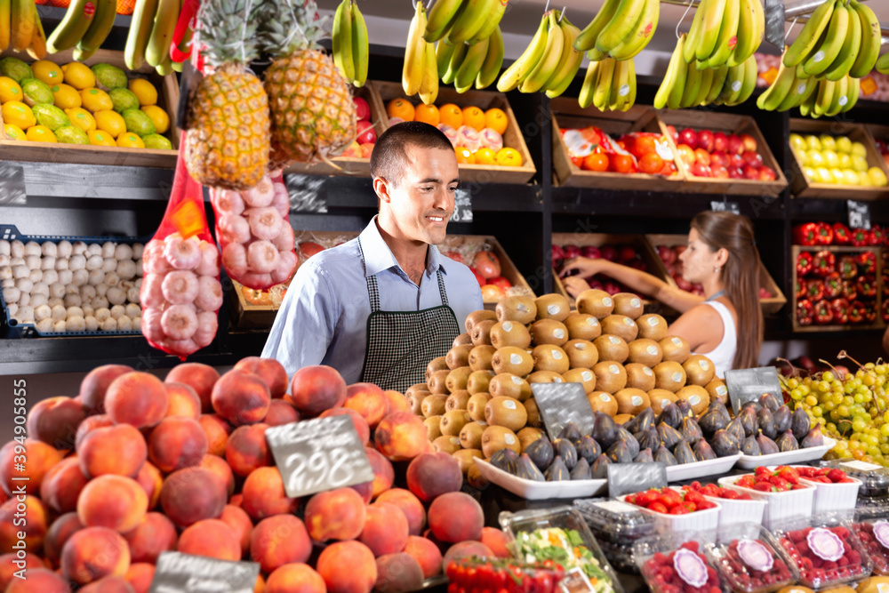 Friendly happy cheerful positive man and woman laying out vegetables and fruits in shop