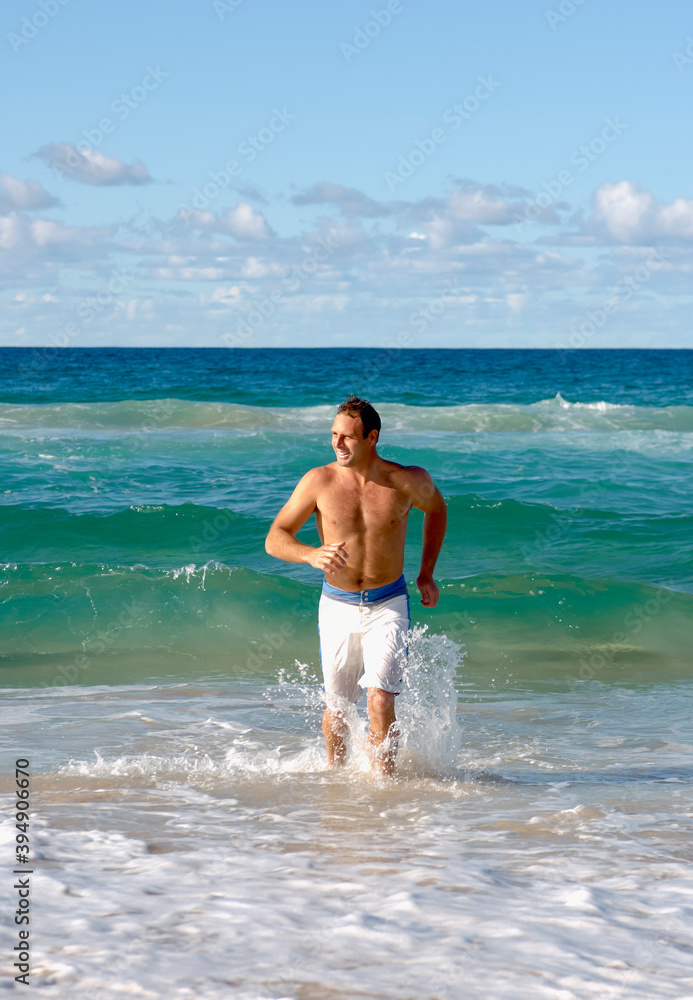 Man in swimming boardshorts running through waves towards sandy beach followed by waves Man in swimming boardshorts running through waves towards sandy beach followed by waves