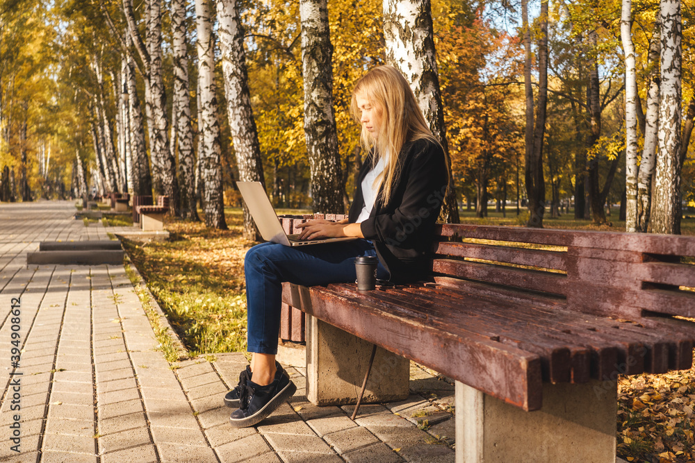 Young businesswoman working on laptop in park with coffee. Autumn park, sunny day. Young businesswoman working on laptop in park with coffee. Autumn park, sunny day.