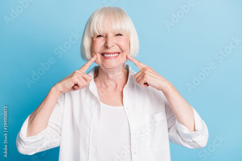 Photo portrait of granny blonde hair pointing at white teeth healthy smile dental whitening veneers isolated on bright blue color background photo