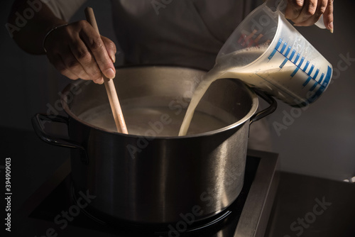 Pouring milk from beaker into metal pot and mixing it with rice to cook rice pudding