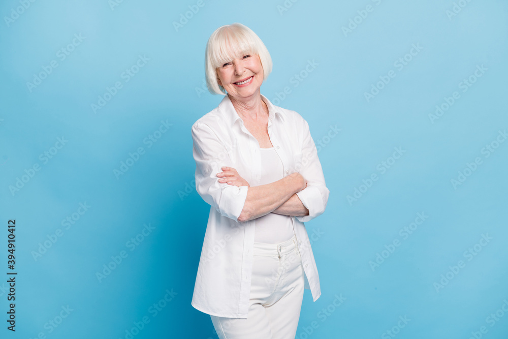 Photo portrait of cute happy old lady with crossed hands wearing white outfit smiling isolated on bright blue color background Photo portrait of cute happy old lady with crossed hands wearing white outfit smiling isolated on bright blue color background