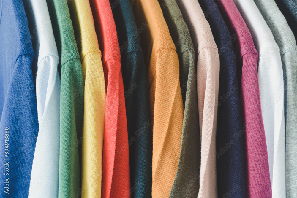 close up collection of colorful t-shirts hanging on clothes hanger in closet or clothing rack