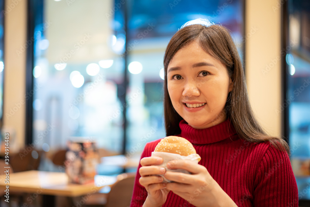 Cheerful Asian woman enjoy eating a grilled meat hamburger in the fast food restaurant at night. Cheerful Asian woman enjoy eating a grilled meat hamburger in the fast food restaurant at night.