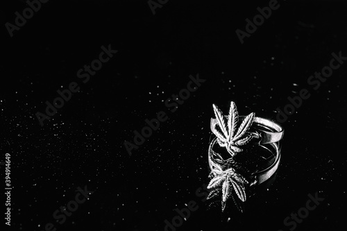 One silver cannabis ring lie on a black background with a mirrored surface. Silver occult jewelry