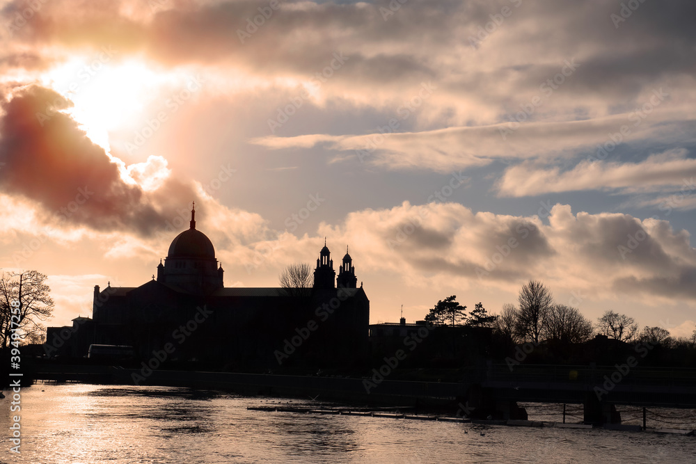 Silhouette of Galway Cathedral against cloudy sky. Galway city, Ireland. View from Corrib river, sea gulls flying in the air.