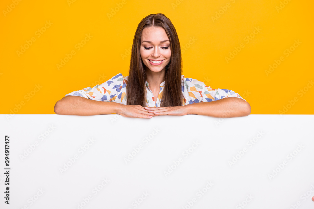 Photo portrait of cute girl looking down at white wall with blank space below hands isolated on vivid yellow colored background Photo portrait of cute girl looking down at white wall with blank space below hands isolated on vivid yellow colored background
