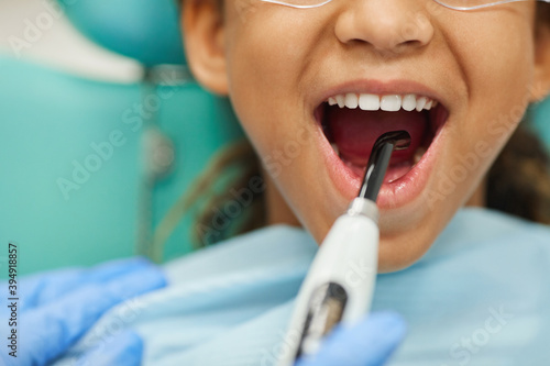 Close-up of little girl opening her mouth while dentist curing her teeth with medical equipment