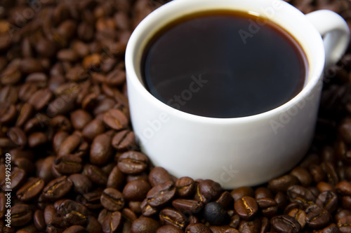 Close-up of coffee cup with roasted coffee beans surrounded by coffee beans