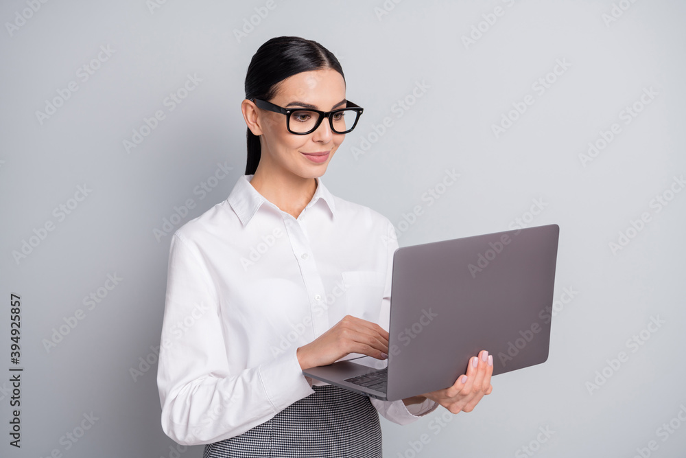 Photo of calm programmer girl hold laptop look screen wear eyeglasses white shirt isolated grey color background Photo of calm programmer girl hold laptop look screen wear eyeglasses white shirt isolated grey color background