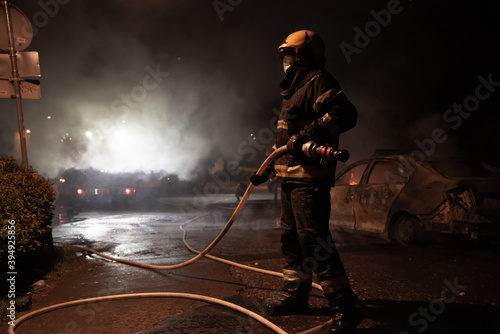 Firefighter trying to put down fire on burning police car in the center of city near church during riots caused by new measures of coronavirus in Belgrade, Serbia, 08.07.2020