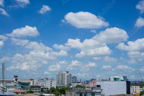 White fluffy clouds on vivid blue sky above a city, view from rooftop 