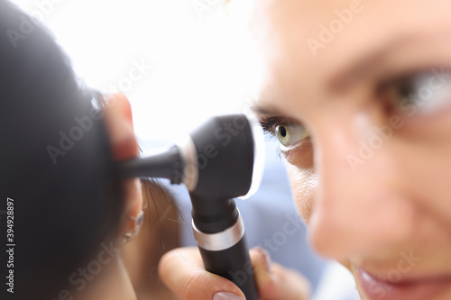 Doctors holding otoscope near patients ear in clinic close-up. Diagnosis of otitis media concept photo