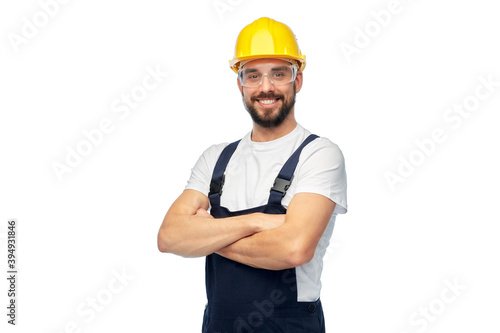 profession, construction and building - male worker or builder in yellow helmet and goggles with crossed arms over white background photo