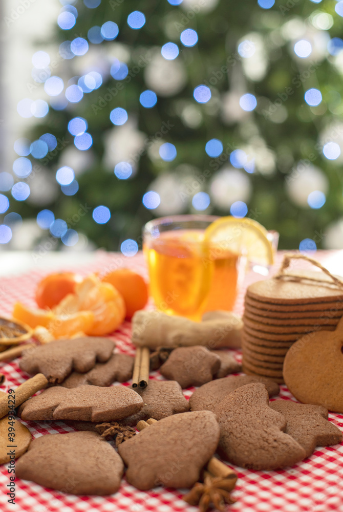 christmas gingerbread cookies and cinnamon on a red checkered tablecloth next to citrus tea and ginger against the background of a christmas tree, vertical position christmas gingerbread cookies and cinnamon on a red checkered tablecloth next to citrus tea and ginger against the background of a christmas tree, vertical position
