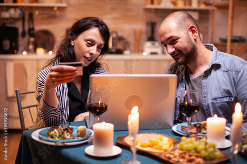 Couple doing shopping online at dinner on laptop. Adults sitting at the table, searching, browsing, surfing, using technology card payment, internet