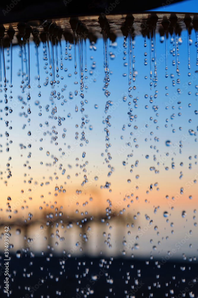 Water pouring from the outdoor beach shower head on blurred sunset seascape background, selective focus