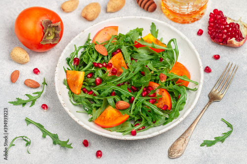 Delicious salad of fresh arugula, persimmon, pomegranate and almonds with a dressing of olive oil and honey. Healthy diet food. Selective focus