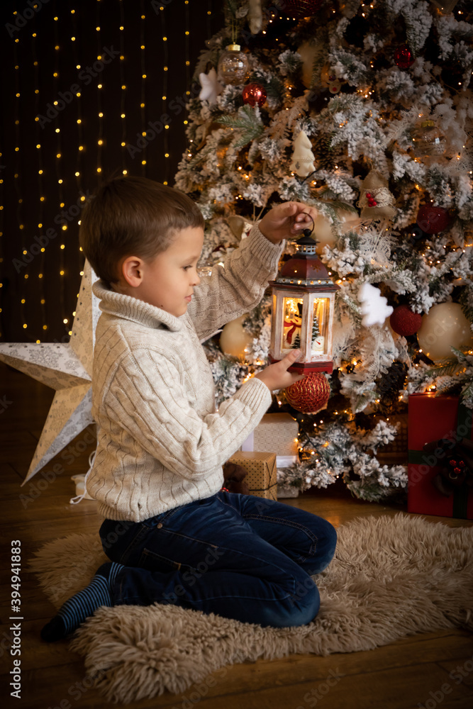 Little boy in holding a white lantern in his hand and sitting near the Christmas tree at home, Happy New year Little boy in holding a white lantern in his hand and sitting near the Christmas tree at home, Happy New year
