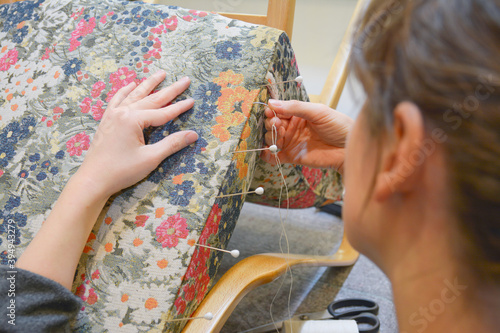 Woman hands sewing with upholstery round needle. Upholsterer working with fabric with flowers pattern. Hand sewing in upholstery workshop. 