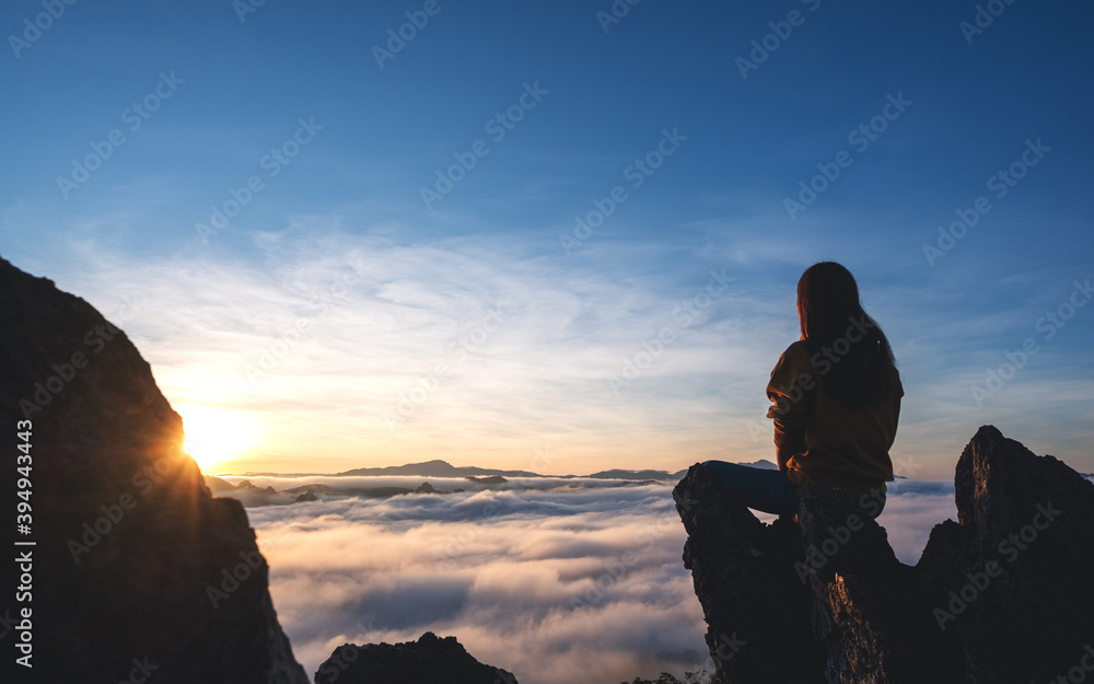 A female traveler sitting on the mountain peak, watching sunrise and sea of fog