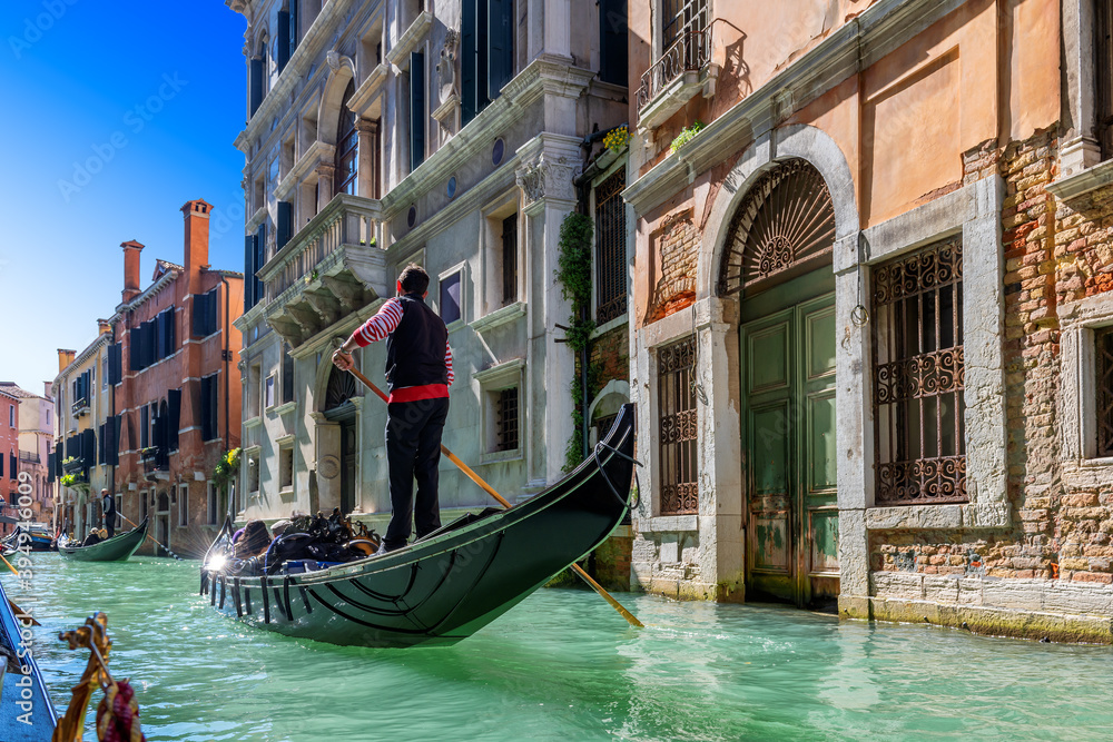 A Venetian gondolier rules a gondola through the waters of the Venice canal, Venice, Italy