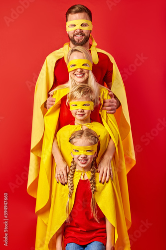 super family in hero cloaks standing isolated on red studio background, brave parent with members of family