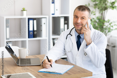 Doctor talking on smart phone with patient, writing notes