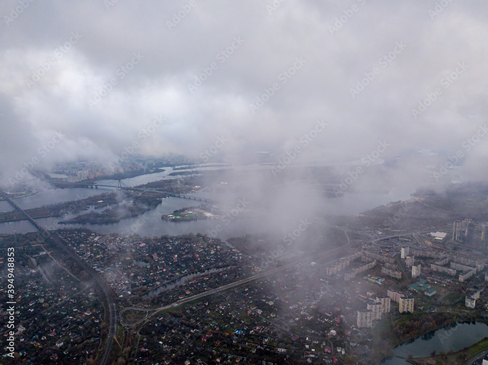 High aerial flight in the clouds over Kiev. An autumn cloudy morning, the Dnieper River is visible on the horizon.