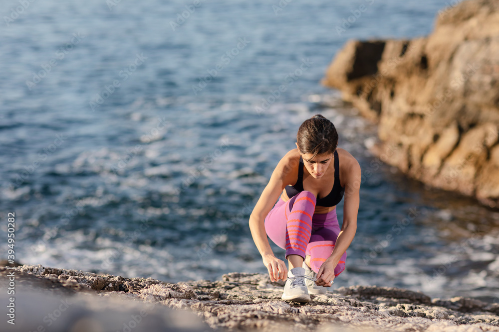 Female runner tying shoes at the beach near the sea. 