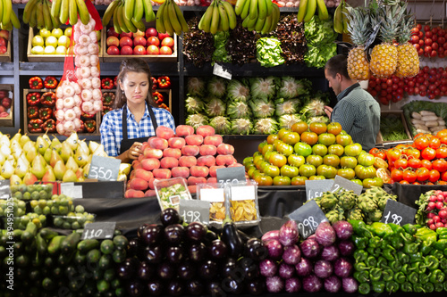 Man and woman shop assistants laying out fruits and vegetables behind the counter in supermarket