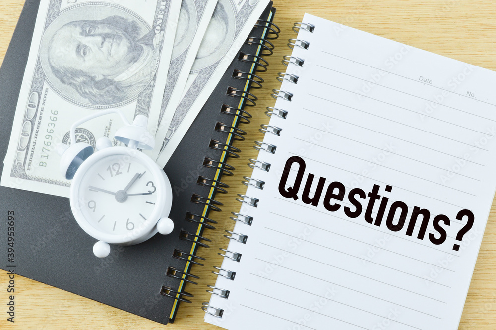 Selective focus of banknote, clock and notebook written with QUESTIONS? over wooden background. Business concept. Selective focus of banknote, clock and notebook written with QUESTIONS? over wooden background. Business concept.