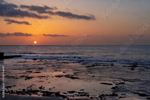 Spectacular sunset with purple hues and calm ocean waves on a wild beach near Palm Mar resort, atmospheric evening with sun dipping into the sea, crepuscular landscape, Tenerife, Canary Islands, Spain
