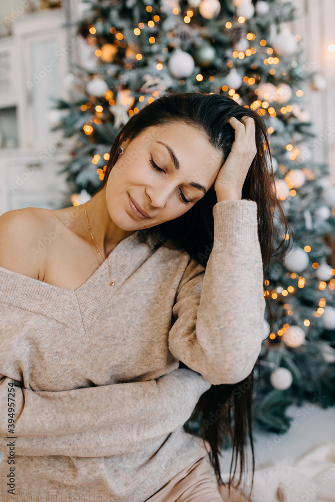 Young brunette woman in sweater, sitting next to a Christmas tree. Young brunette woman in sweater, sitting next to a Christmas tree.