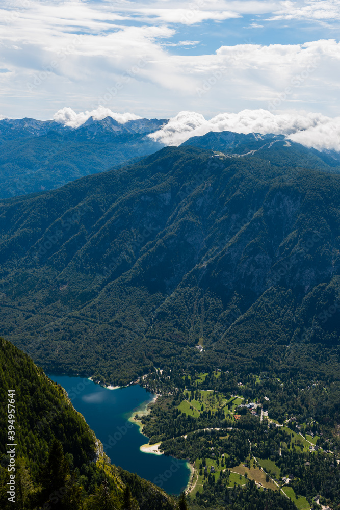 Standing on top of the mountain Planina Blato in the Triglav National Park in Slovenia looking down on Lake Bohinj and the village Ukanc on sunny day with clouds