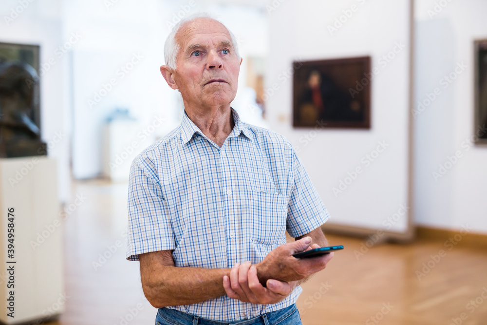 mature European man examines paintings in an exhibition in hall of an art museum mature European man examines paintings in an exhibition in hall of an art museum