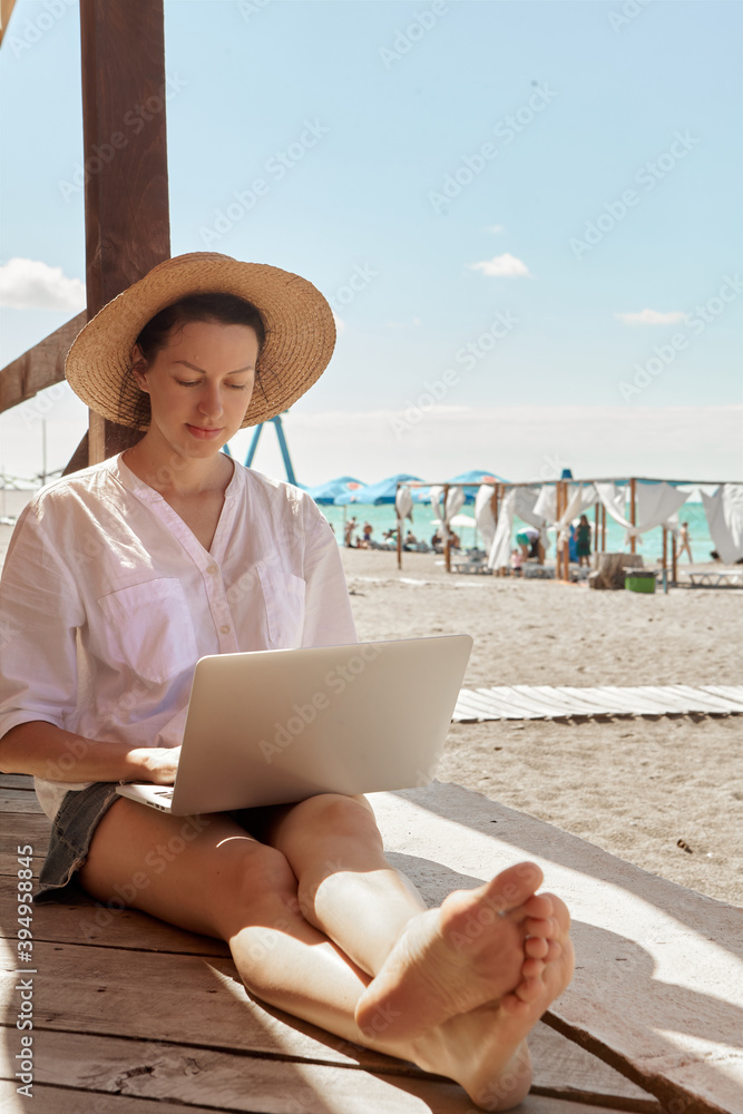 Young woman using laptop computer on a beach. Freelance work concept..Pretty young woman using laptop in cafe on tropical beach in outdoor cafe terrace with sea view. Work and travel