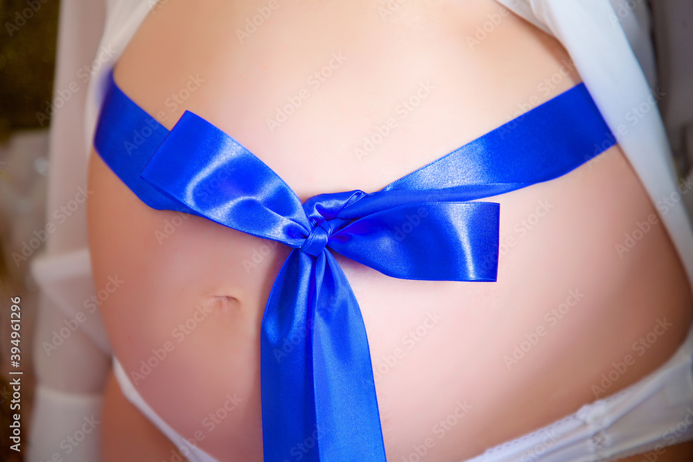 Pregnant belly with blue ribbon. The concept of waiting for a child, happy motherhood, third trimester. Pregnant belly with blue ribbon. The concept of waiting for a child, happy motherhood, third trimester.
