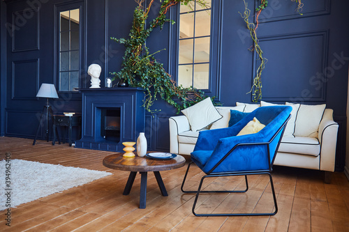 Modern interior of a spacious living room with contrasting blue walls and wooden floors, a blue armchair and a white sofa. The concept of art Nouveau style, a real photo of the interior.