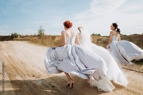 Crazy bride with her two friends running on a sandy path