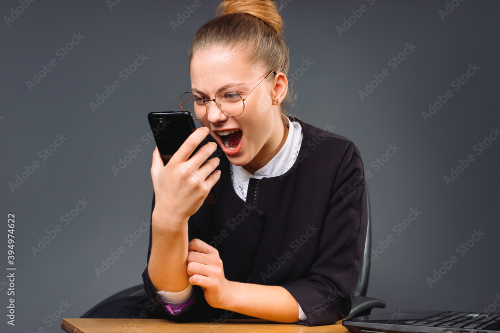 Young, serious boss woman, nervously shouting into the phone. Gray background. Young, serious boss woman, nervously shouting into the phone. Gray background.