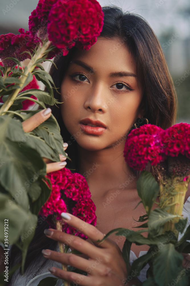 closeup portrait of a beautiful young Thai woman surrounded by red flowers. Spring blossom